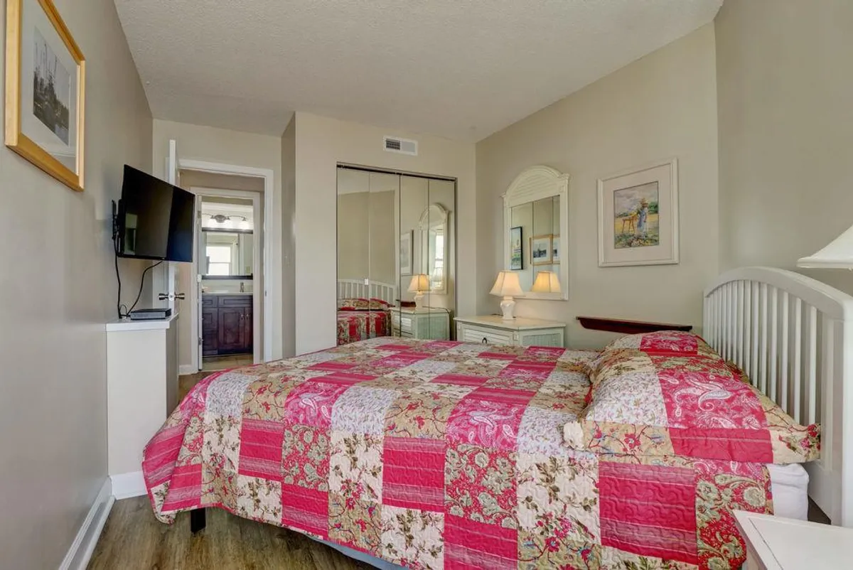A cozy bedroom showcasing a bed with a patchwork quilt, mirrored closet doors, nightstands with lamps, and framed artwork. The soft lighting and inviting atmosphere evoke relaxation and comfort.