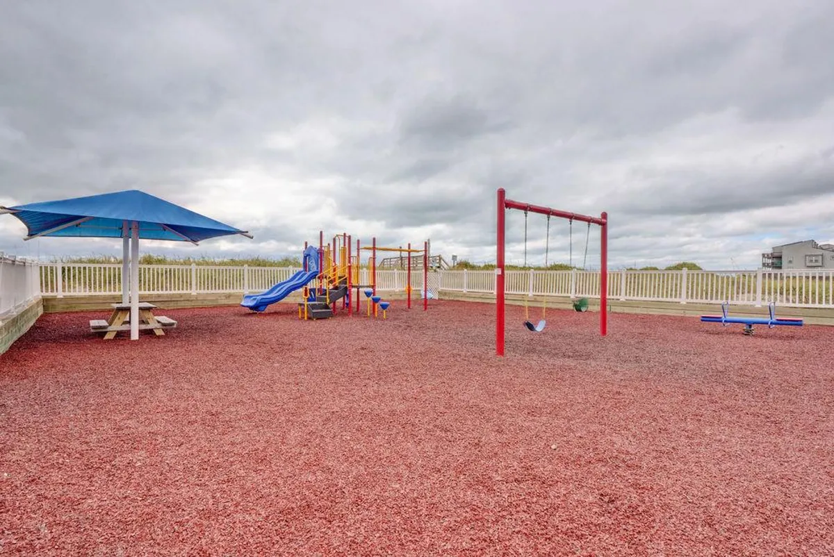 A bright, inviting playground featuring slides, swings, and a picnic table shaded by a canopy. Children can be seen playing energetically, while families gather for picnics in the sunny outdoor setting. The scene conveys a safe and exciting environment for younger guests.