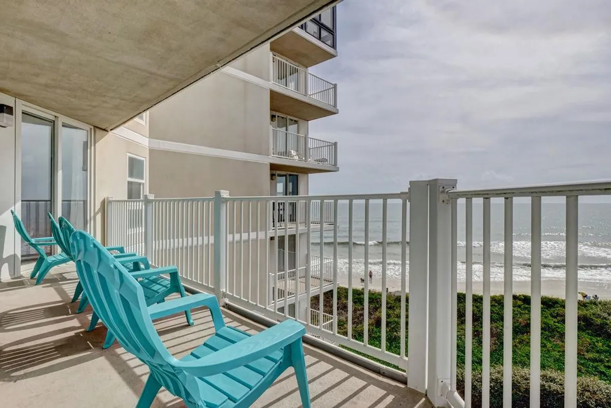 This image captures a tranquil beachfront view with turquoise chairs positioned perfectly to enjoy the ocean waves. The scene evokes peaceful moments spent watching the sun rise or set, feeling the ocean breeze, and relaxing together on the private balcony.