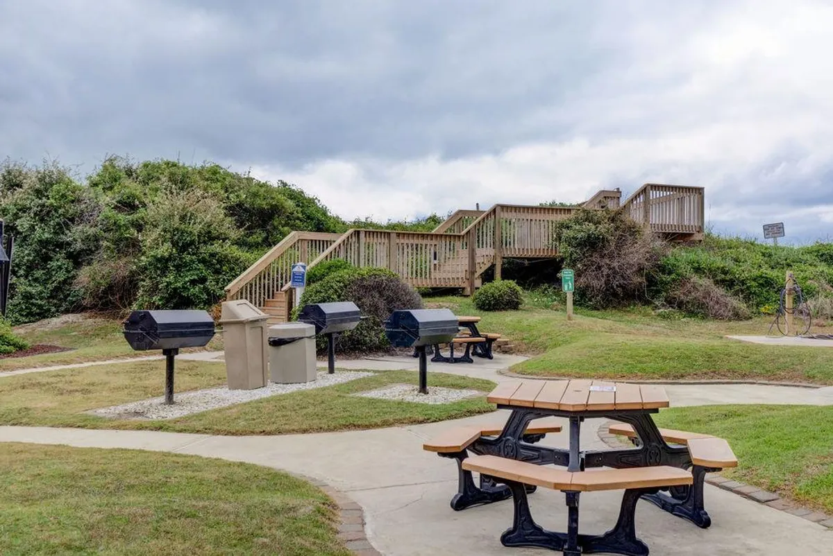 A casual outdoor space with picnic tables, barbecue grills, and wooden stairs leading up, set in a communal area ideal for cookouts and gatherings. The setting is well-suited for relaxed family barbecues or group meals after a day of adventure.