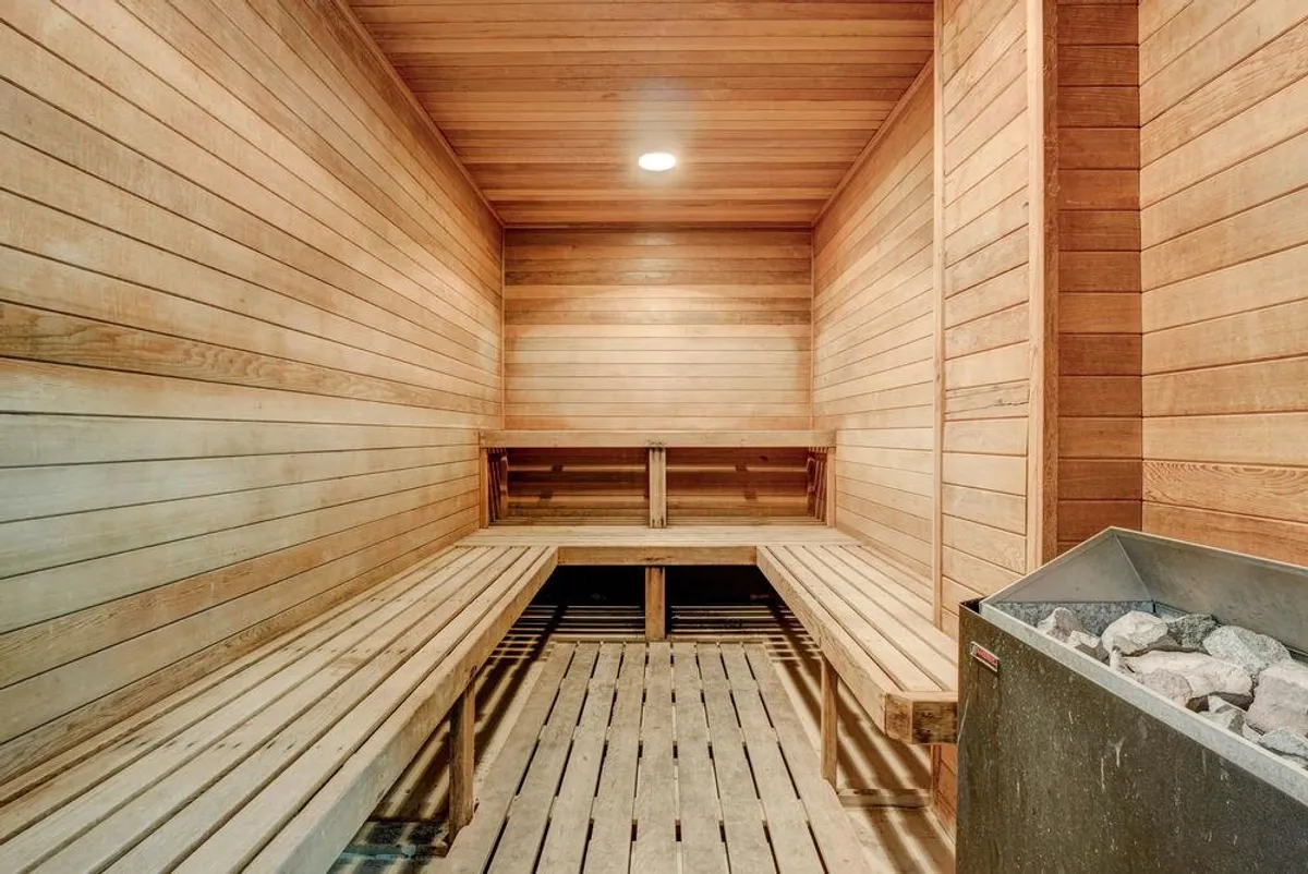 A serene sauna room featuring wooden benches and a traditional sauna heater, creating a calm, inviting space for relaxation and detoxification. The warm wood tones evoke spa-like tranquility.