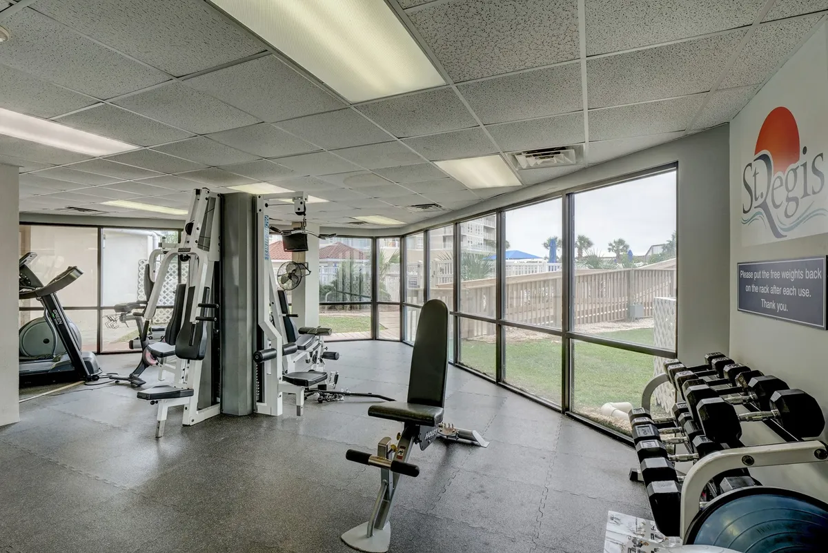 A well-equipped fitness center featuring exercise machines, free weights, and expansive windows that let in natural light. The mood is energetic and motivating, suited for those seeking wellness during their stay.