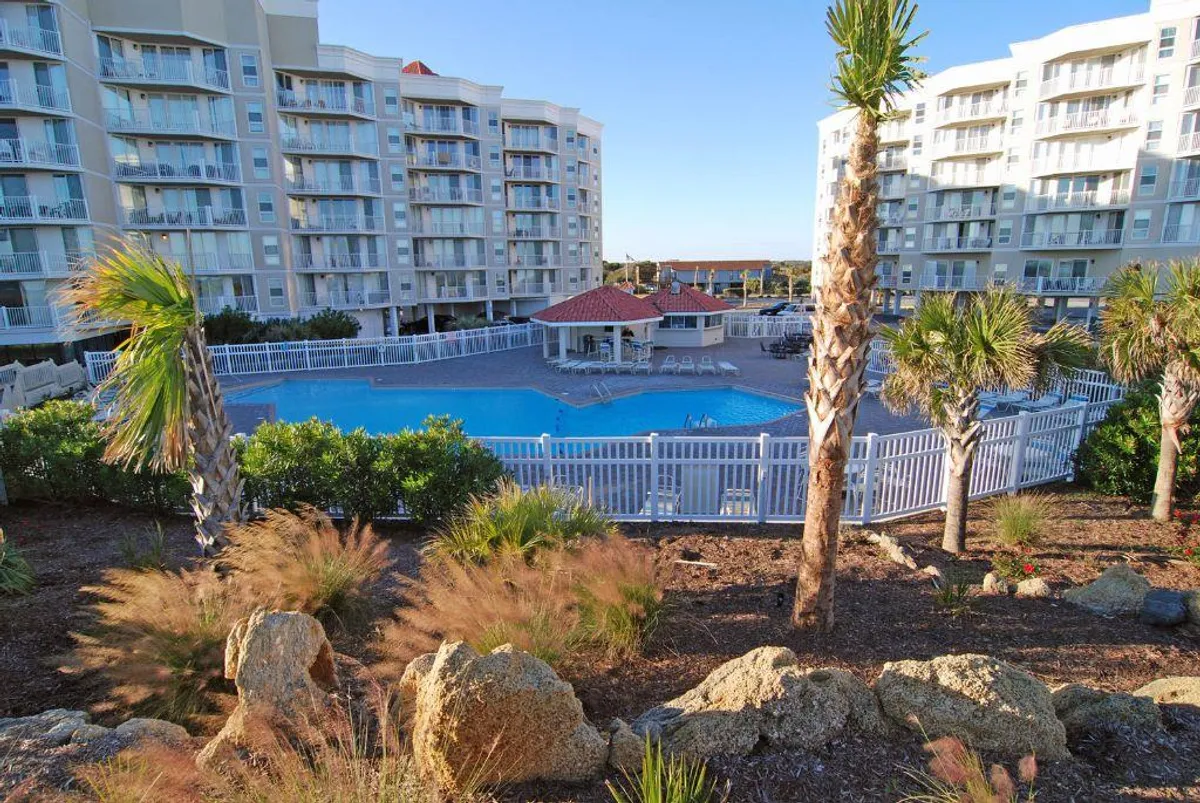 This image showcases a sparkling swimming pool surrounded by palm trees, with landscaped gardens and nearby buildings in the background. The pool is the central feature, inviting guests for a swim or to lounge poolside in a relaxing atmosphere.