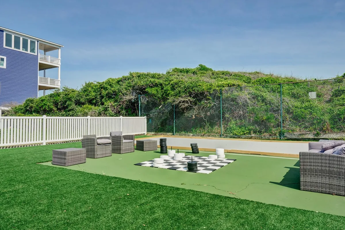 A vibrant outdoor chessboard sits at the center of a green lawn, surrounded by inviting seating and a secure perimeter. The playful scene encourages friendly competition, laughter, and bonding outdoors—capturing the spirit of shared recreation.