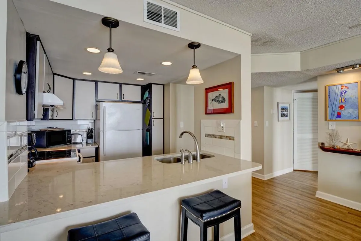 A stylish, modern kitchen featuring a central island with bar stools, pendant lighting, and eye-catching wall art. The setup highlights both the functional and social aspects of the kitchen, with ample counter space for meal prep and casual dining. The scene feels welcoming and contemporary, ideal for hosting or sharing meals.
