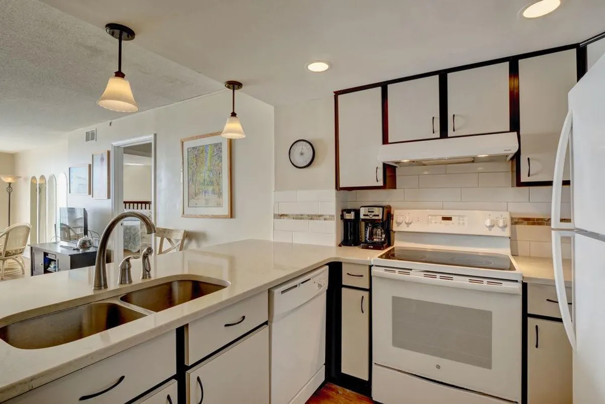 A close-up of the kitchen's modern appliances and a spacious countertop, framed by warm lighting and decorative art. The stainless steel sink and modern features underline the space's practicality and readiness for any culinary adventure. This image brings attention to the appliances and the generous workspace available to guests.